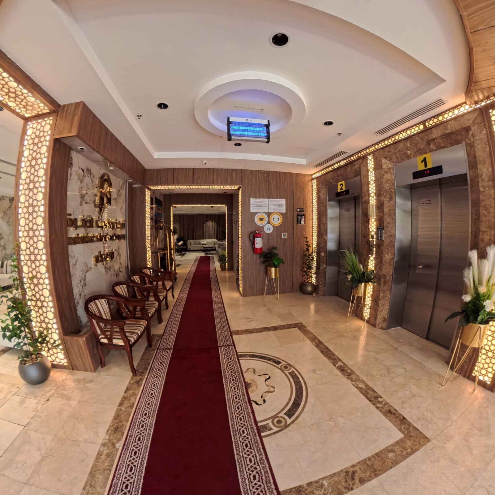 Um saguão de hotel com carpete vermelho, painéis de madeira e dois elevadores.