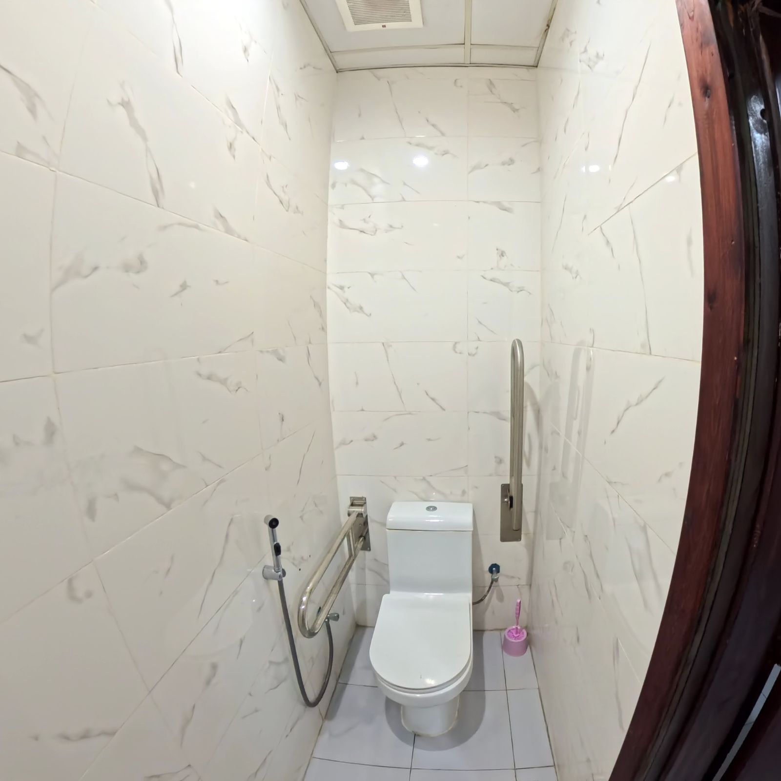 Een kleine, praktische badkamer met toilet, een handgreep en bediening voor de douche.