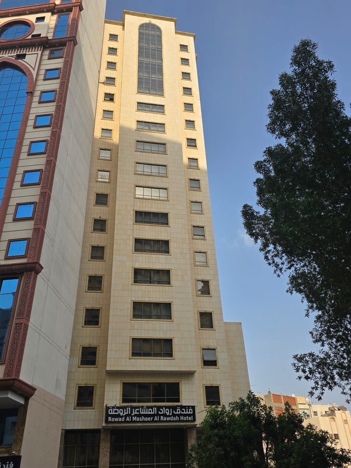 A tall hotel building with multiple floors and a sign indicating it is the Rowad Al Mashaer Al Rawdah Hotel.