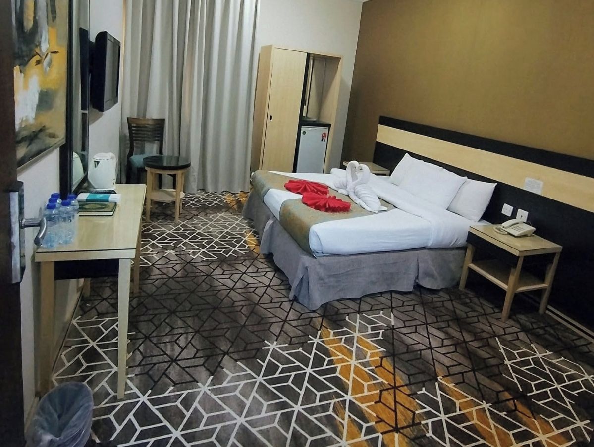 Een hotelkamer met een bed, nachtkastje, klein bureau, stoel, kledingkast en een televisie.