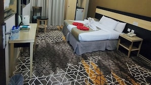Una habitación de hotel con cama, mesita de noche, un escritorio pequeño, una silla, armario y televisor.