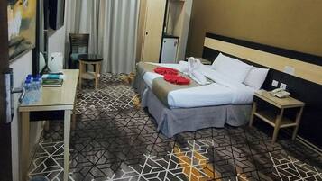 Een hotelkamer met een bed, nachtkastje, klein bureau, stoel, kledingkast en een televisie.