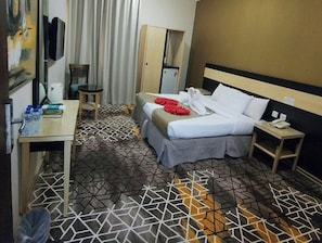 Ein Hotelzimmer mit Bett, Nachttisch, kleinem Schreibtisch, Sessel, Kleiderschrank und Fernseher.