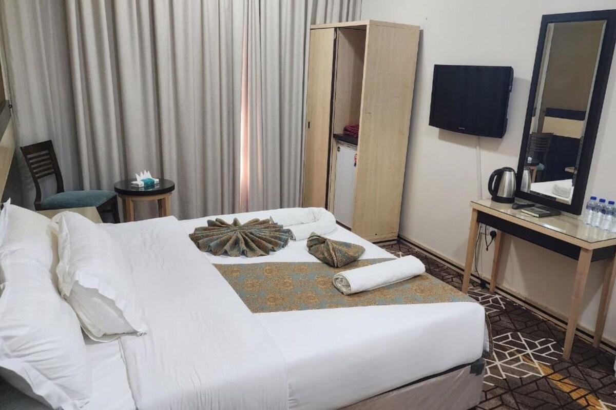 A hotel room with a bed, a desk, a chair, a television, and a wardrobe.
