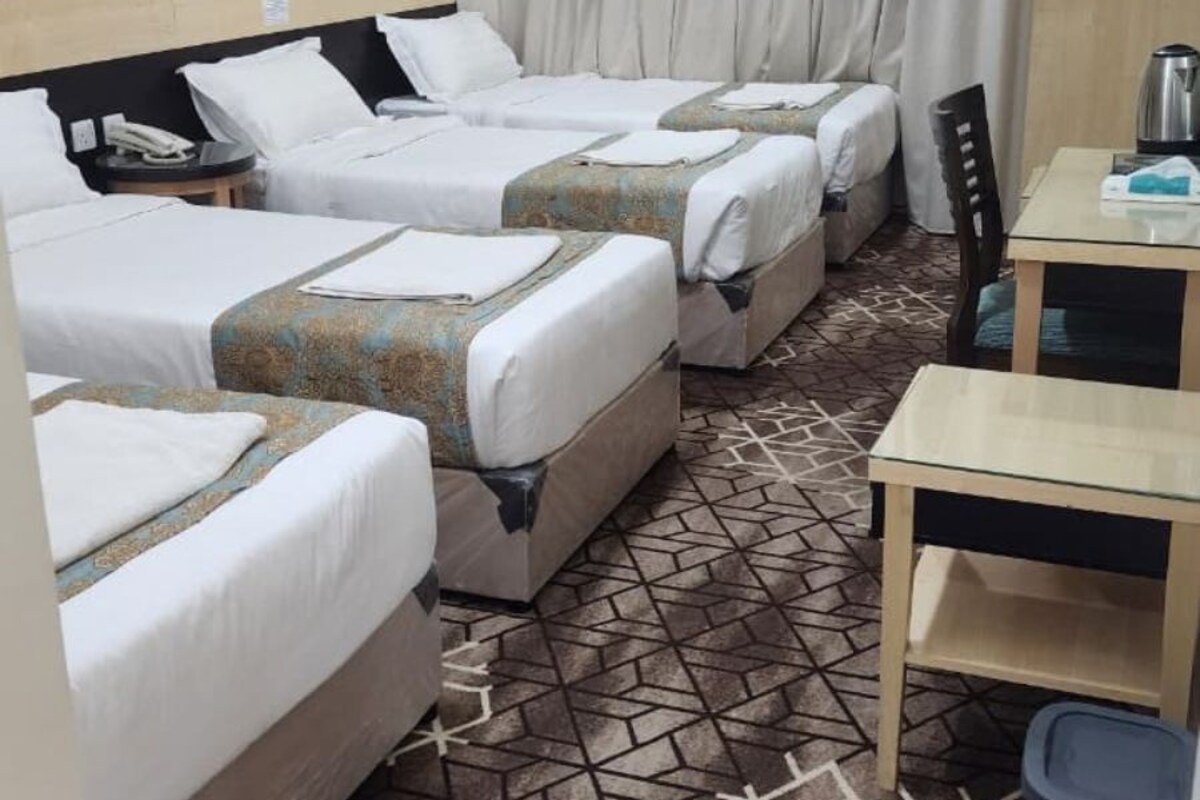 A hotel room with three beds, a small table, a chair, and a trash bin.