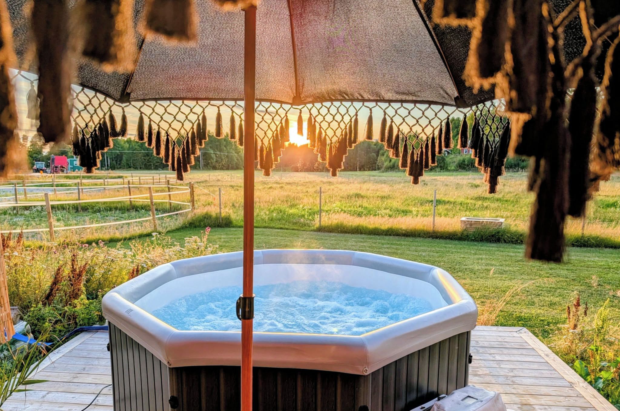 A hot tub in a garden with a wooden deck, surrounded by grass and a fence.