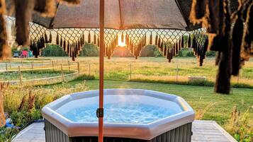 Un jacuzzi en un jardín con terraza de madera, rodeado de césped y una valla.