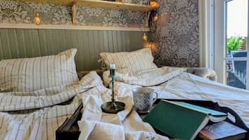 Una cama bien hecha con ropa de cama a rayas, una mesita de noche con una lámpara y una ventana con vistas a la vegetación.