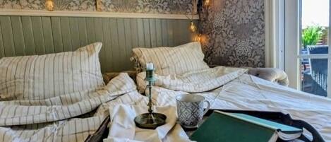 Un lit bien fait, avec une literie à rayures, une table de chevet avec une lampe et une fenêtre donnant sur un paysage verdoyant.