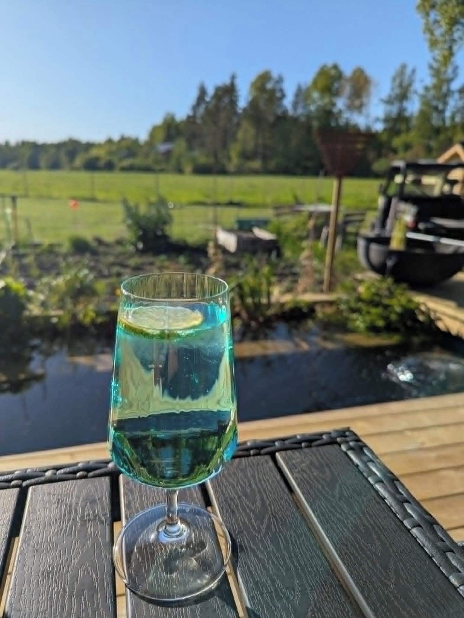 A glass of clear liquid with a slice of lime on a wooden table outdoors.