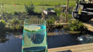 A glass of clear liquid with a slice of lime on a wooden table outdoors.