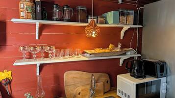 Una cocina con pared roja, repisas blancas, una lámpara colgante, un tostador, un microondas y un lavamanos.