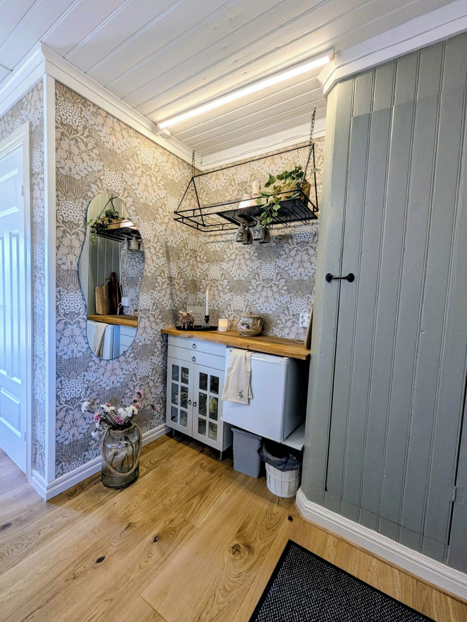 Ett badrum med ett handfat i trä, en spegel, en hängande växt och ett skåp.