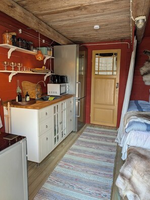 A compact kitchen with a microwave, kettle, and various utensils on shelves.