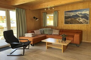 Un intérieur en bois comprenant un canapé, un fauteuil, une table et un tableau représentant un paysage de montagne.