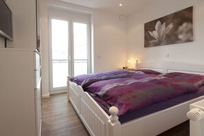 Ein Schlafzimmer mit einem Bett, einem Fenster und einem an der Wand hängenden Bild.