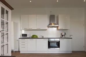 Eine moderne Küche mit weißen Schränken, einer eingebauten Mikrowelle, einem Edelstahlbackofen und einer Edelstahl-Dunstabzugshaube.