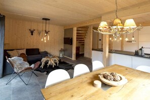 A modern interior with a wooden dining table, white chairs, a sofa, and a kitchen area. - Cabin with 1 bedroom (St. Georgen am Kreischberg)