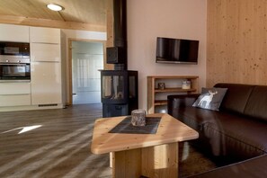 A modern living room with a wooden table, a leather sofa, a television, and a wood-burning stove. - Cabin with 1 bedroom (St. Georgen am Kreischberg)