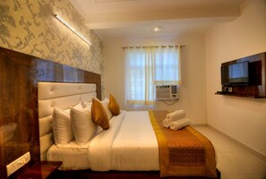 A hotel room with a bed, a television, an air conditioning unit, and a window with curtains. - HOTEL KAVYA INN  (New Delhi)