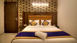 Ein Hotelzimmer mit einem Holz-Kopfteil, Wandtapete mit Muster, einem Bett mit blauer und goldener Bettdecke und einem weißen Handtuch auf dem Bett.