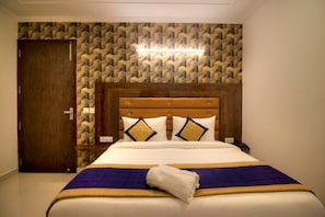 Une chambre d’hôtel avec une tête de lit en bois, un papier peint à motifs, un lit recouvert d’une courtepointe bleue et dor ée, et une serviette blanche posée sur le lit.