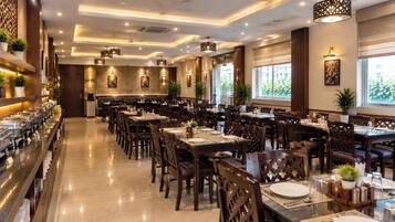 A spacious dining area with multiple tables and chairs, a buffet line on the left, and large windows allowing natural light.
