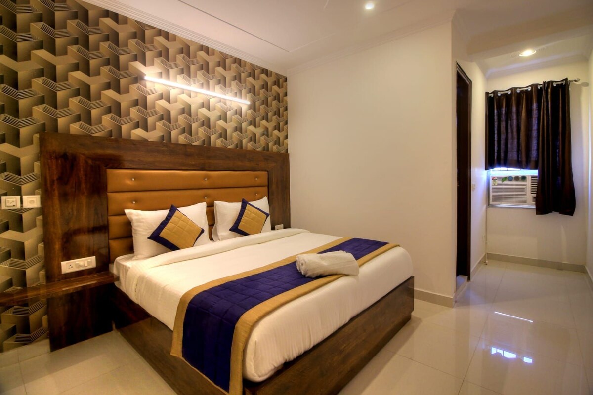A hotel room with a bed, a headboard, a wall with a geometric pattern, and a window with curtains.