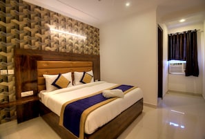 Une chambre d’hôtel avec un lit, une tête de lit, un mur orné d’un motif géométrique et une fenêtre avec des rideaux.