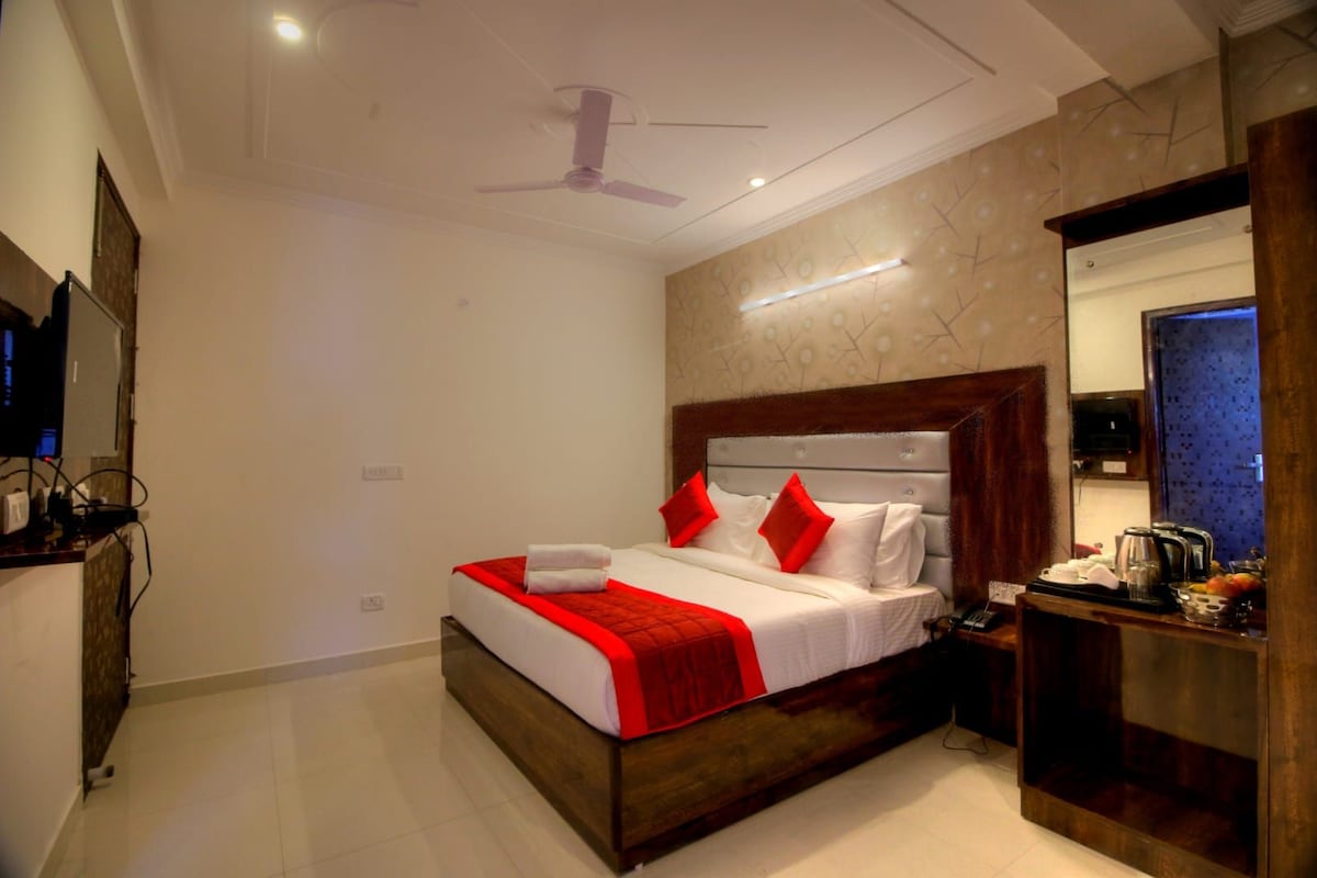 Une chambre d’hôtel équipée d’un lit, d’une table de chevet, d’un miroir, d’un ventilateur de plafond et d’un téléviseur fixé au mur.