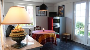 A kitchen with a dining table, a lamp, a fruit bowl, a refrigerator, and a window with a view. - Between Land & Sea – Ocean View and Private Garden in Ciboure (Ciboure)