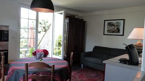 A living room with a sofa, a dining table with chairs, a flower vase, a lamp, and a painting on the wall. - Between Land & Sea – Ocean View and Private Garden in Ciboure (Ciboure)
