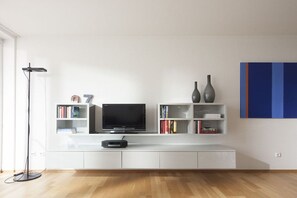 A modern living room with a flat-screen TV, white cabinetry, and a floor lamp. - Apartment 9, Südstrasse 1 (Norderney)