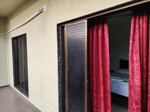 A room with a bed, a window with a metal grill, and a red curtain.