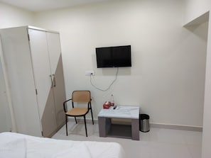 Ein Zimmer mit einem Bett, einem Kleiderschrank, einem Schreibtisch mit Stuhl, einem Fernseher und einem Mülleimer.
