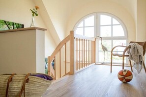 A room with a wooden floor, a white door, a wooden railing, a wicker chair, and a basketball. - ||------------------------Reed Warbler 48--------------------|| (Fuhlendorf)