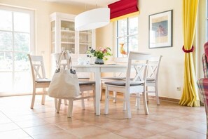 A dining area with a white table, chairs, a hanging light fixture, and a window with yellow curtains. - ||------------------------Reed Warbler 48--------------------|| (Fuhlendorf)