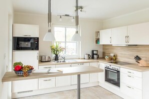 A modern kitchen with white cabinetry, a built-in microwave, a stove, and pendant lighting. - Holiday home with 2 bedrooms (Fuhlendorf)