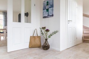 A hallway with a white door, a woven bag, and a vase with flowers. - Holiday home with 2 bedrooms (Fuhlendorf)
