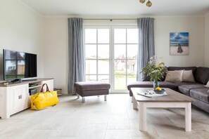 A modern living room with a television, sofa, coffee table, and a large window with curtains. - Holiday home with 2 bedrooms (Fuhlendorf)