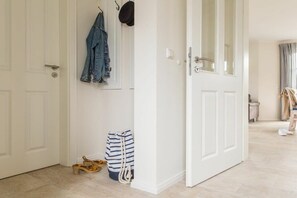 A hallway with a white door, a hanging jacket, and a striped bag on the floor. - Holiday home with 2 bedrooms (Fuhlendorf)
