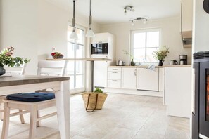 A modern kitchen with white cabinetry, a microwave, a stove, and a dining area with a table and chairs. - Holiday home with 2 bedrooms (Fuhlendorf)