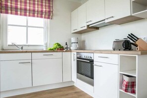 A modern kitchen with white cabinets, a built-in oven, a coffee maker, and a window with a plaid valance. - Holiday home with 2 bedrooms (Fuhlendorf)