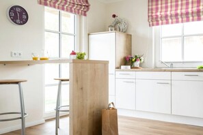 A modern kitchen with a wooden island, bar stools, white cabinets, and a window with a view. - Holiday home with 2 bedrooms (Fuhlendorf)