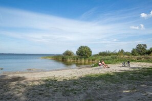 A beach with a clear sky, two people sitting on chairs, and a bicycle. - Holiday home with 2 bedrooms (Fuhlendorf)