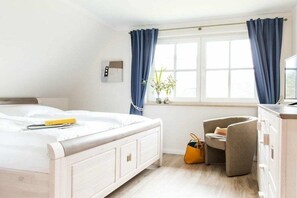 A hotel room with a bed, a desk, a chair, a window with curtains, a plant, and a wall-mounted light switch. - Holiday home with 2 bedrooms (Fuhlendorf)