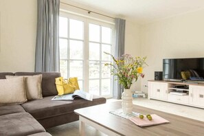A living room with a sofa, a coffee table, a TV, and a window with curtains. - Holiday home with 2 bedrooms (Fuhlendorf)