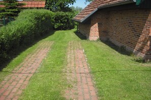 A brick building with a sloped roof, surrounded by a well-maintained lawn and a hedge. - Holiday apartment with 1 bedroom (Carinerland OT Neu Karin)