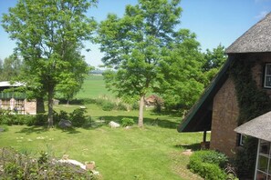 Une propriété rurale comprenant une maison en briques, une construction à toiture de chaume et une cour verdoyante avec des arbres.