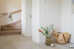 Eine Treppe führt zu einer Tür, eine Vase mit Blumen und eine gewebte Tasche auf dem Boden.